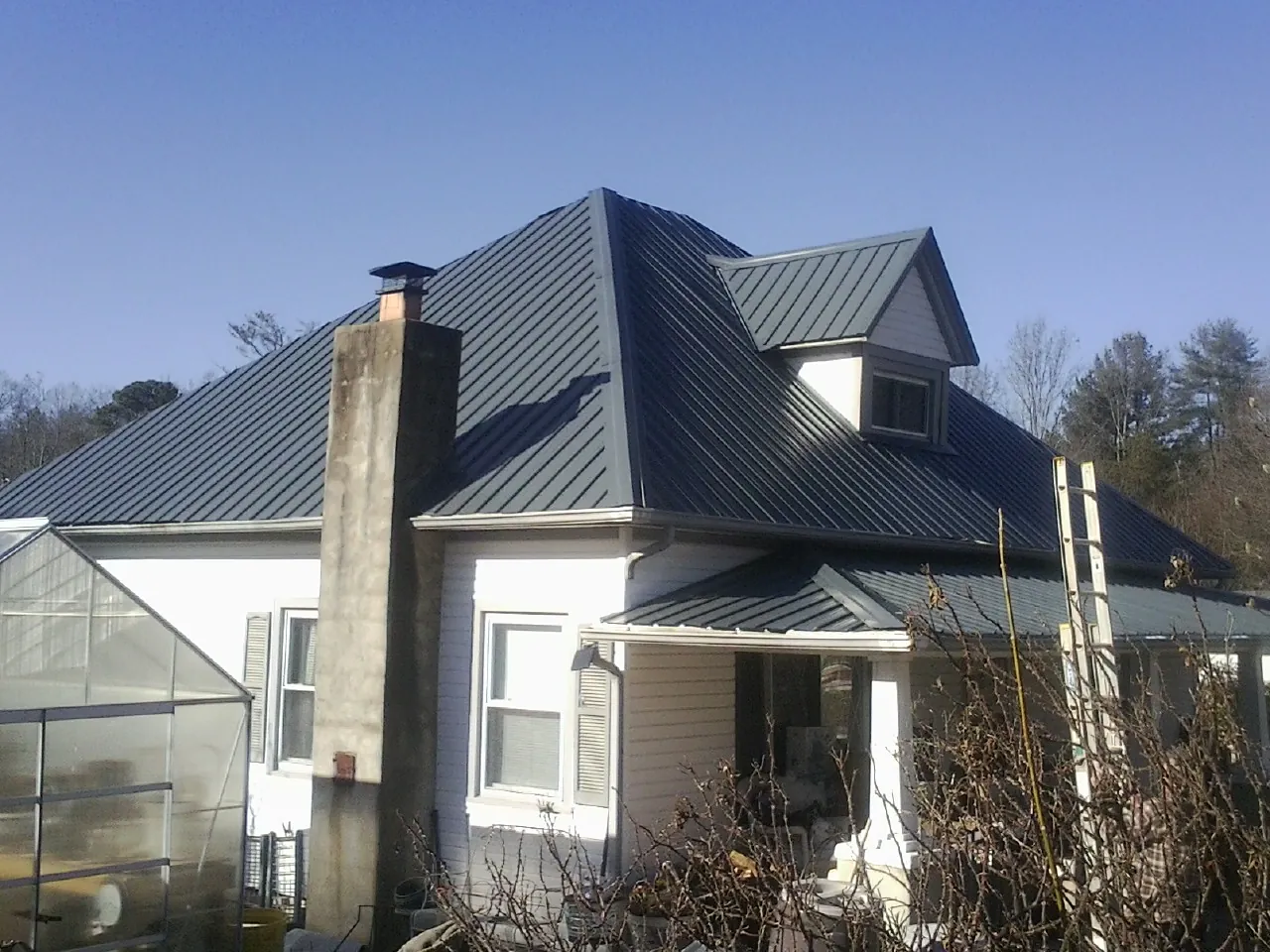Dark blue standing seam metal roof on a white farmhouse with dormer — Slate & Tile Roof Repair by Roofing Brothers in Magnolia